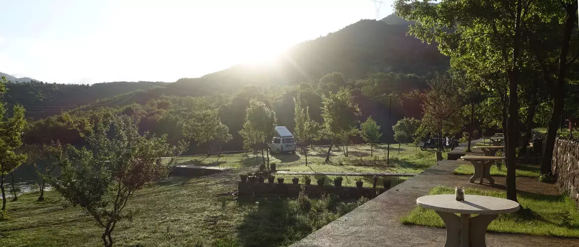 agora camping, agora farmhouse camping, Campingplatz in Albanien, Terasse mit Tischen, große Grünfläche, ein Wohnmobil, im Hintergrund Berge und die aufgehende Sonne