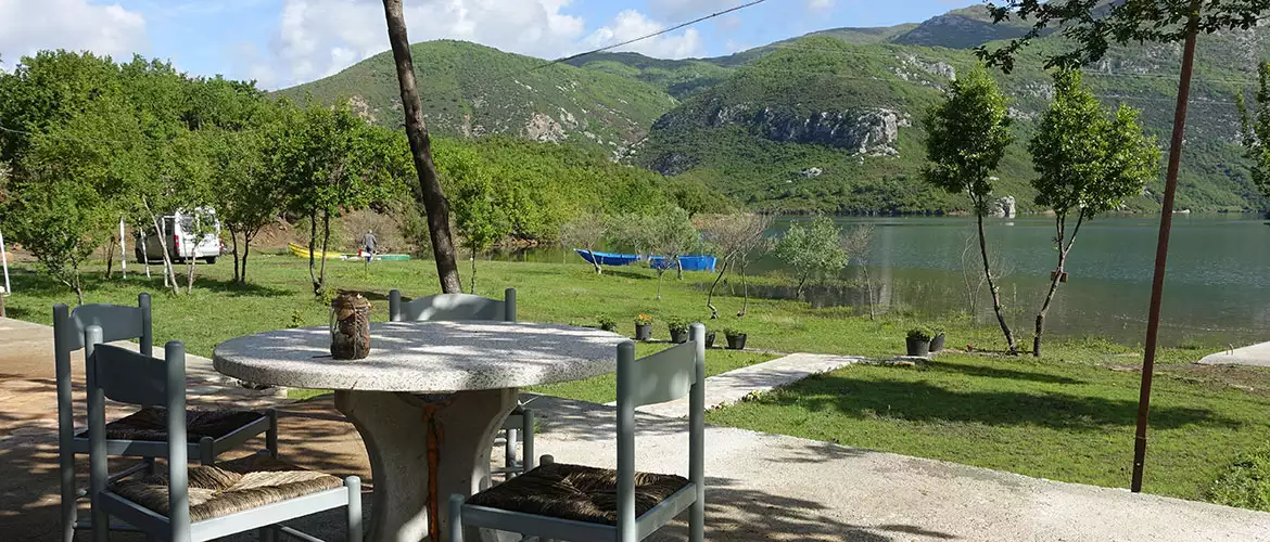 agora camping, agora farmhouse camping, Campingplatz in Albanien, Blick auf den See von der Terasse aus, zwischen See und Terasse eine große Grünfläche, auf der Terasse ein Tisch mit Stühlen, im Hintergrund, Berge